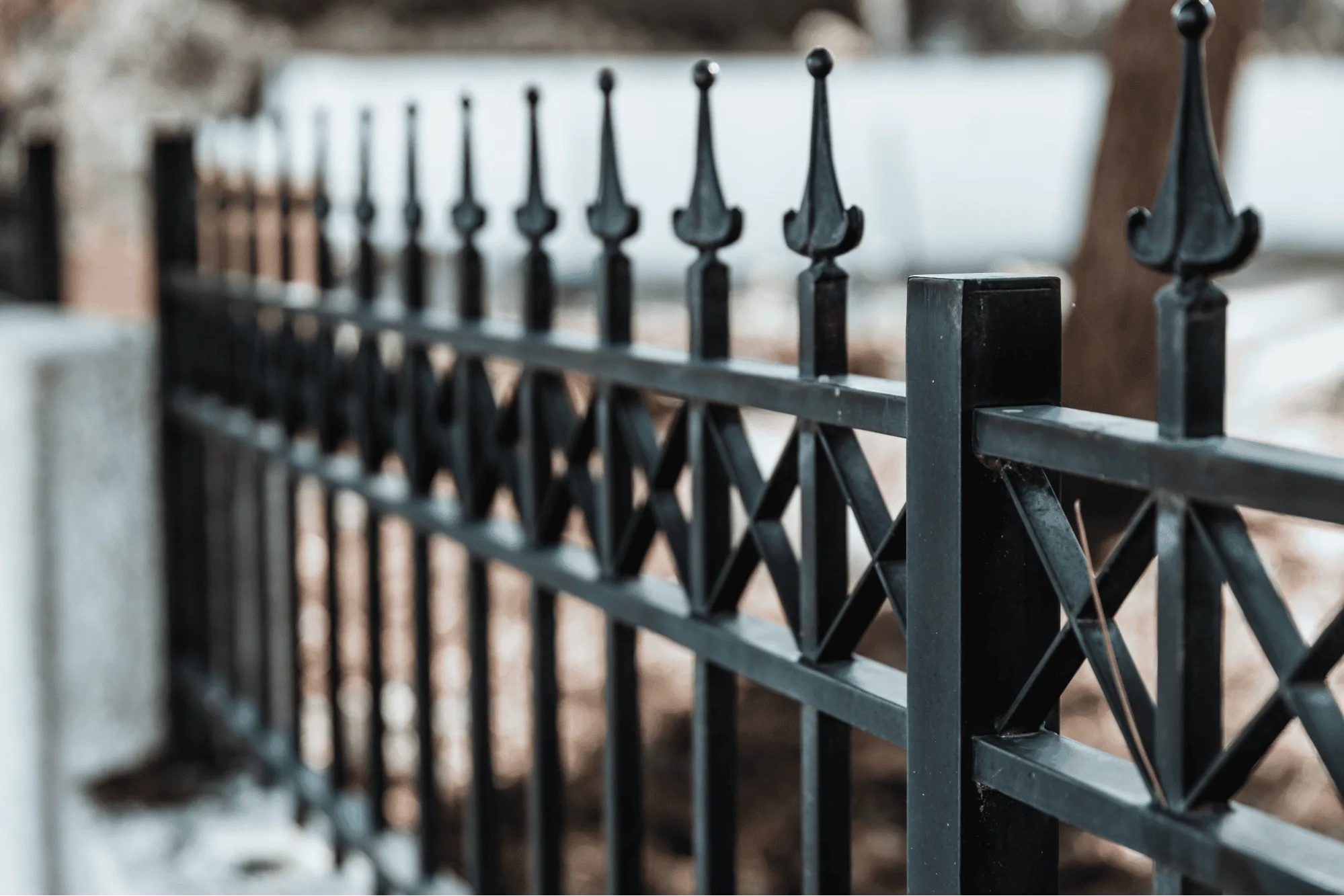 A close-up view of a decorative black steel fence featuring cross-pattern designs and elegant finials. Modern ornamental systems utilize a durable powder-coated finish to protect the metal from the elements, providing a low-maintenance solution for homeowners.