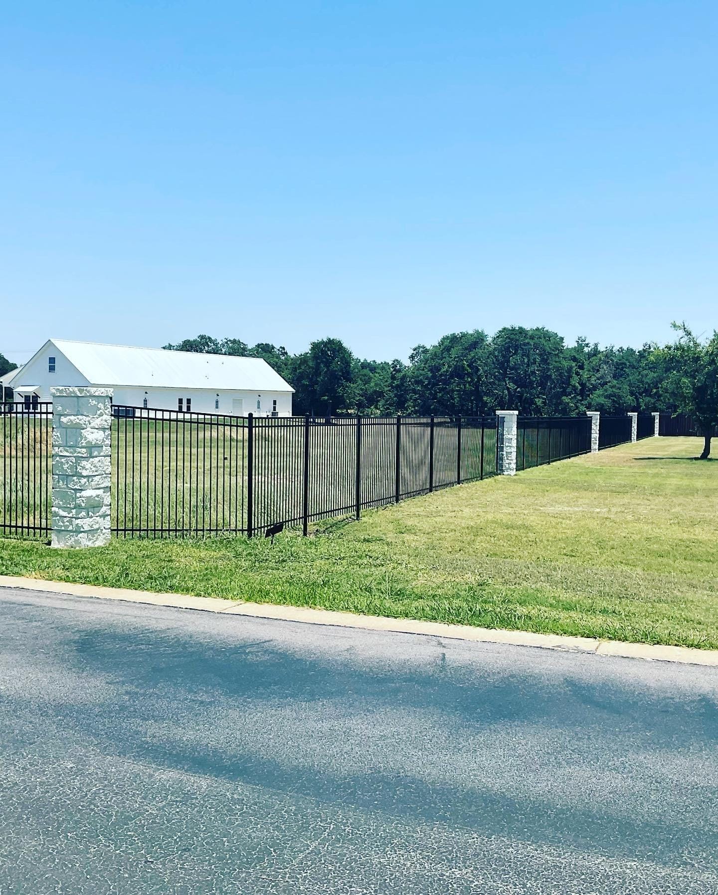 A black ornamental steel fence with stone columns running along a large property boundary, illustrating durable material choices for new fence construction in Georgetown, TX.